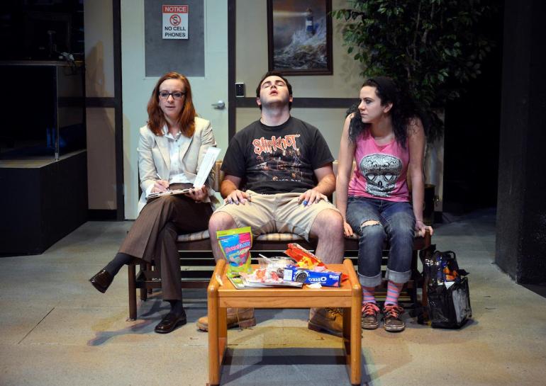 three cast members sit in what looks like a waiting room