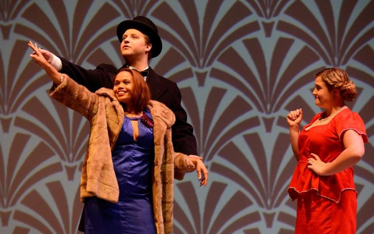 male and female cast members on stage dance with other cast member watching