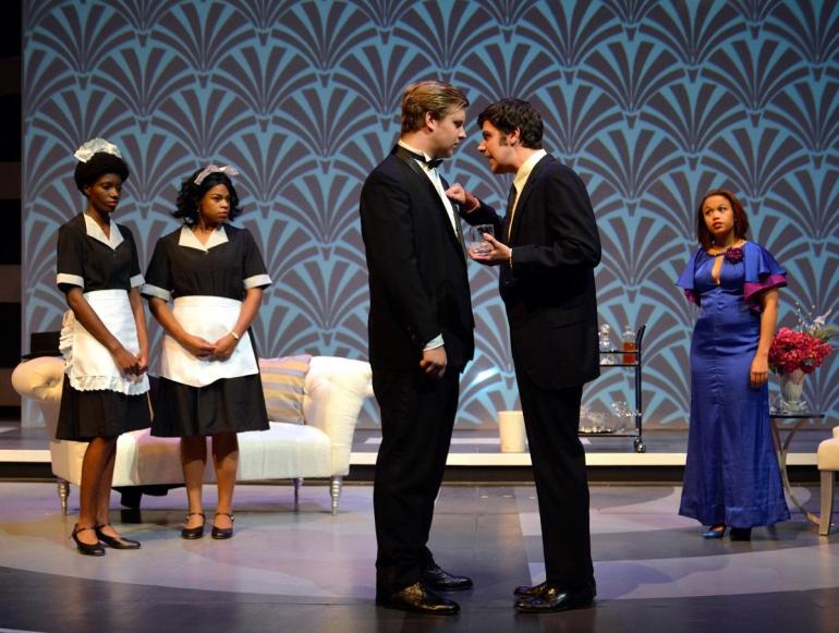 two cast members stand head to head center stage, other cast members watch 