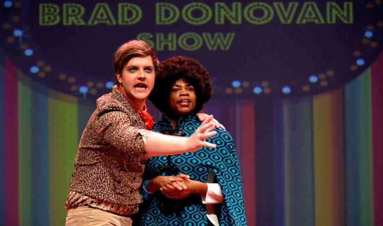 male and female cast member stand closely on stage 