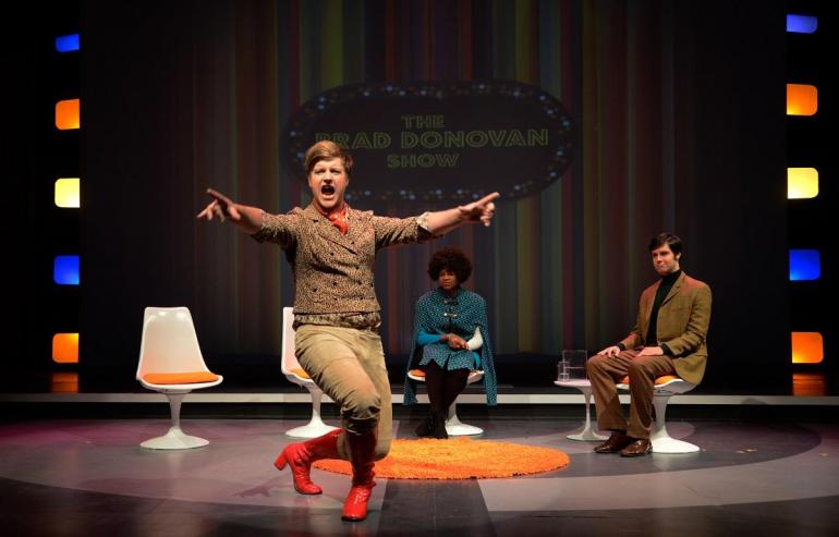 Cast member at center stage dancing, with other cast members watching