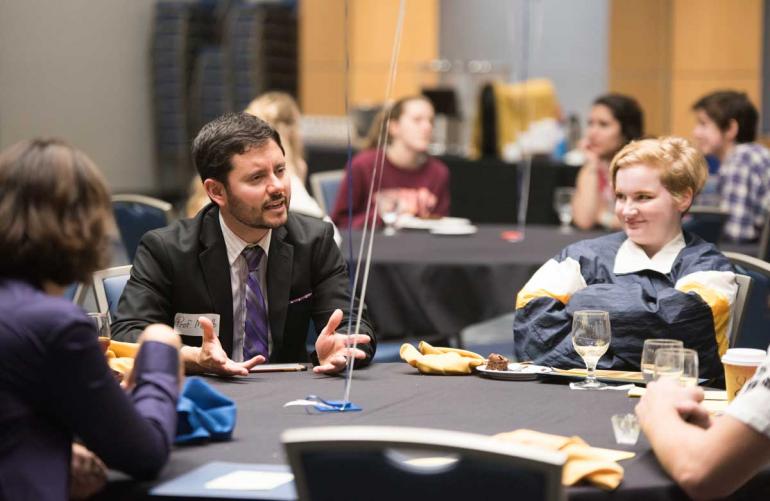 Professor and students talking around a table during a luncheon