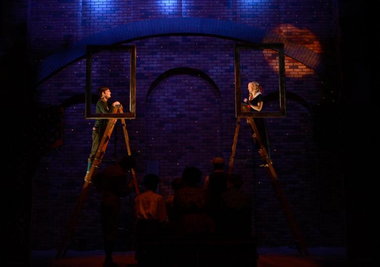 cast members stand on ladders with darkened stage