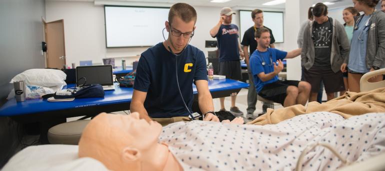 PT Classroom Sim Student observing the still body of a sim mannequin in anxious anticipation due to the lack of a heartbeat