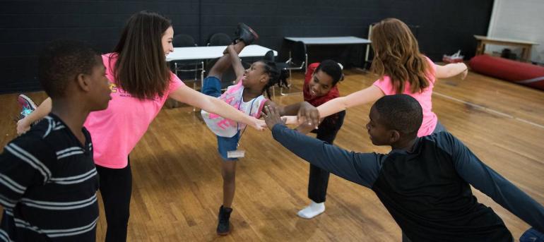 Elementary students lean in and put their hands together 