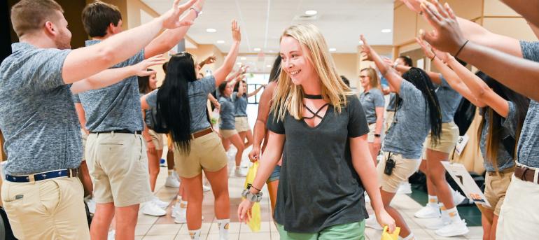 Student walking through a passage created by orientation leaders' arms