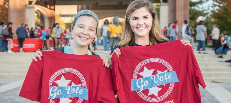 two female students holding Mocs go vote shirts in hand