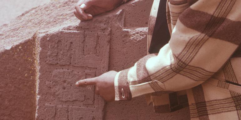 A man's hand points to an incised figure on an ancient Latin American ruin.