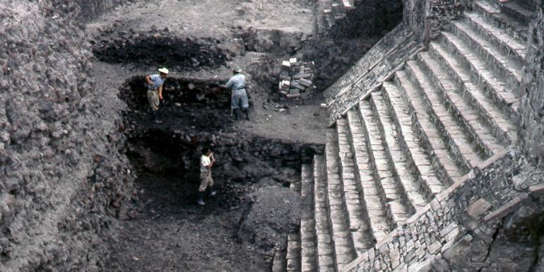 Three men use shovels to excavate the steps of an ancient Latin American monument. 