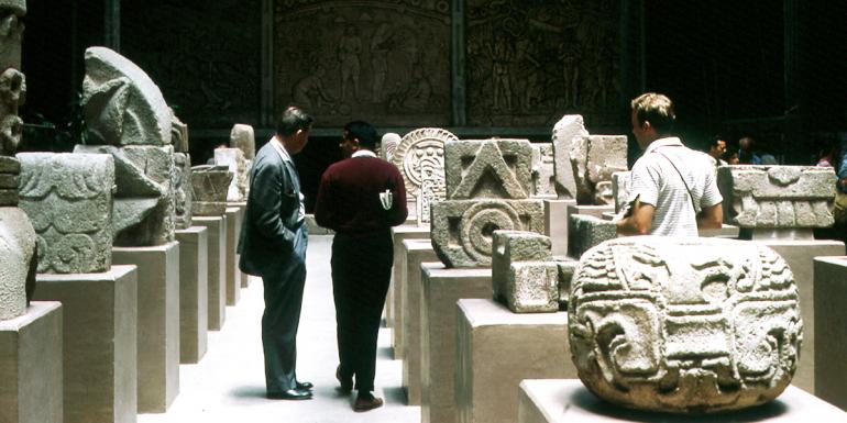 Interior of Museo Victor Emilio Estrada displaying ancient Latin American stone sculptures incised with various motifs.Three men discuss the sculptures.