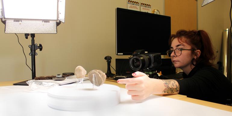 Woman photographing several figurines in the George and Louise Patten collection of Salem Hyde papers and cultural artifacts collection.