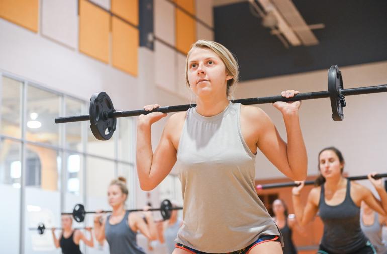 Girl with a cardio barbell doing squats in a group fitness class.