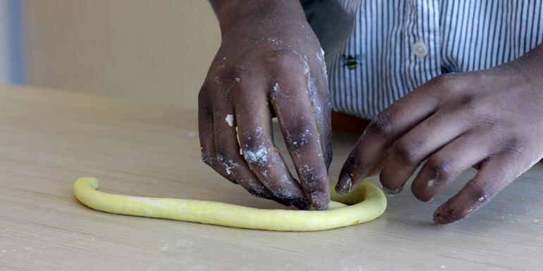 Hands coiling yellow clay into a circle.