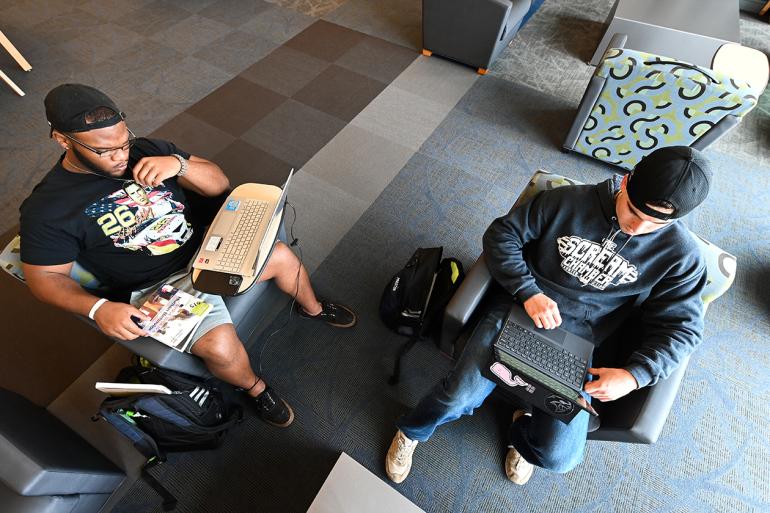 An overhead image of 2 male students, studying the screens of their laptops