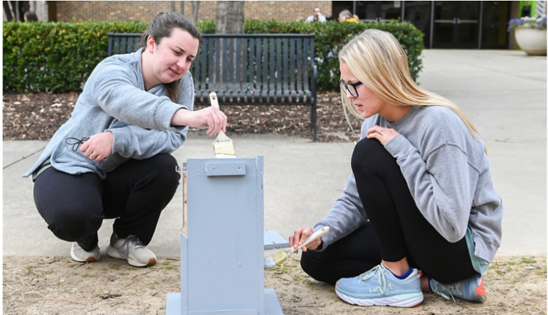 Two students sitting on the ground and painting a bird’s nest 