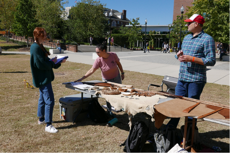 Three students gathered around a table displaying ancient hunting tools.