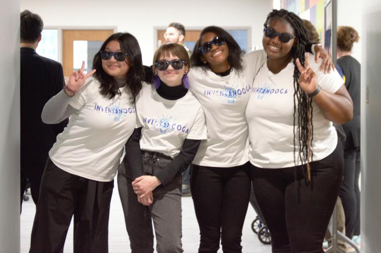 Four students show off branded Inventanooga t-shirts and sun glasses while assisting with Inventanooga, a program designed to inspire young entrepreneurs.