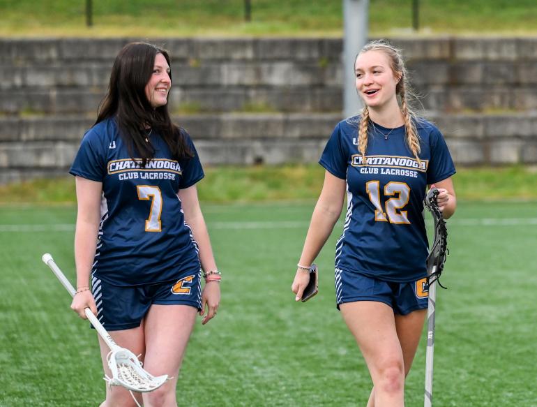 Two female lacrosse players in uniform on the field