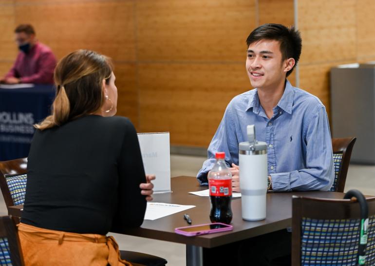 Student in a blue button down shirt talking with a woman in a black jacket.