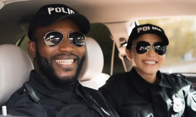 Two police officers, a woman and a man, smile inside a police vehicle.