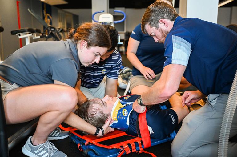 Athletic Training students are spine-boarding a patient during class. Athletic Training students are spine-boarding a patient during class.