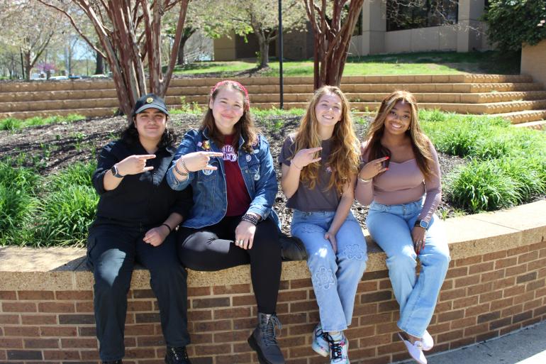 Four students sitting on a bench and making a Power C hand gesture