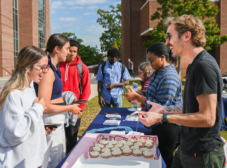 students standing at a bake sale table with cupcakes