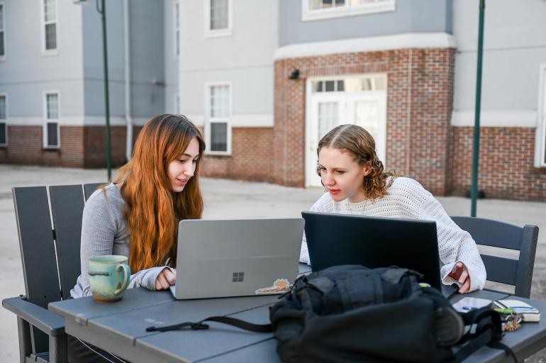 two students working on laptops outside in a courtyard