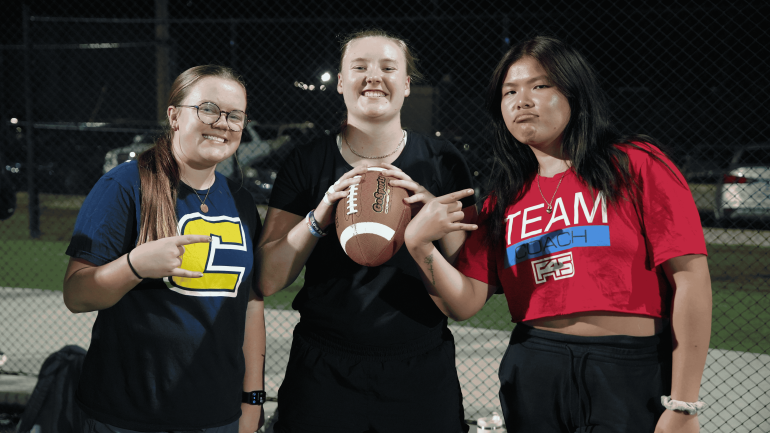 Three women, two holding up the power c and one holding a football.