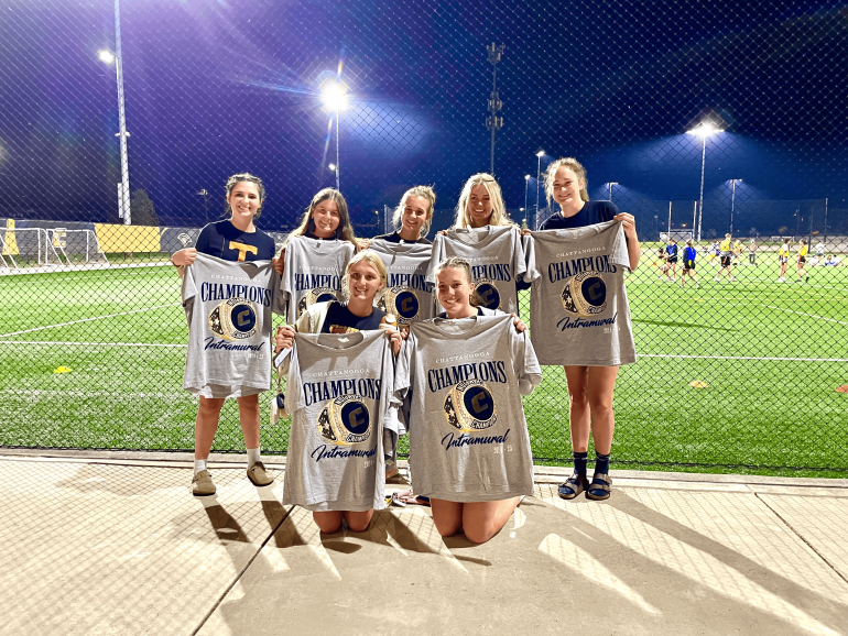 A team of 7 women holding up their intramural championship t-shirts. 