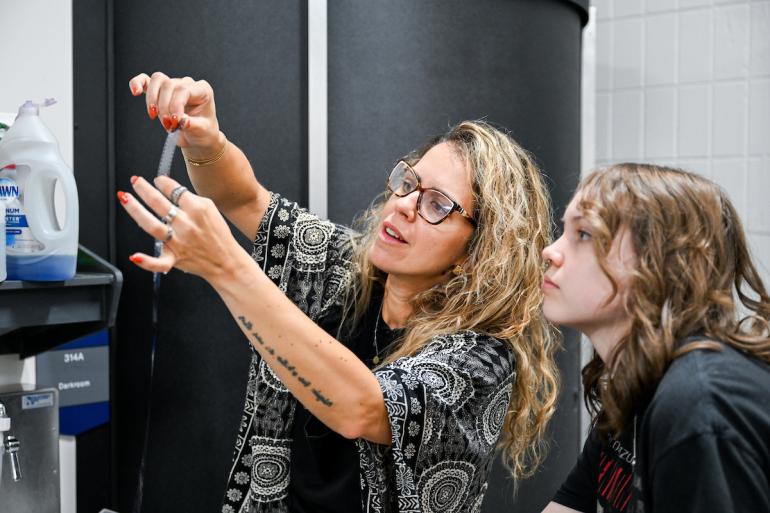 Professor Júlia Pontés reviews a film strip with a student in Photography I