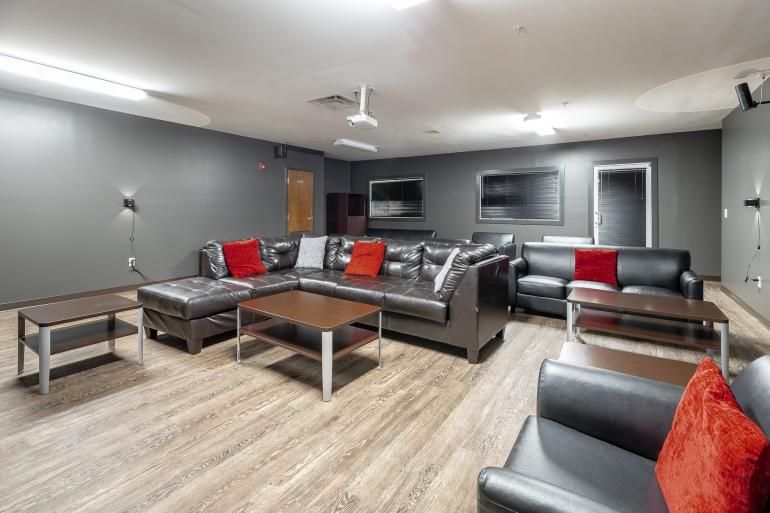 Gray theater room with black couches and end tables and red decorative pillows