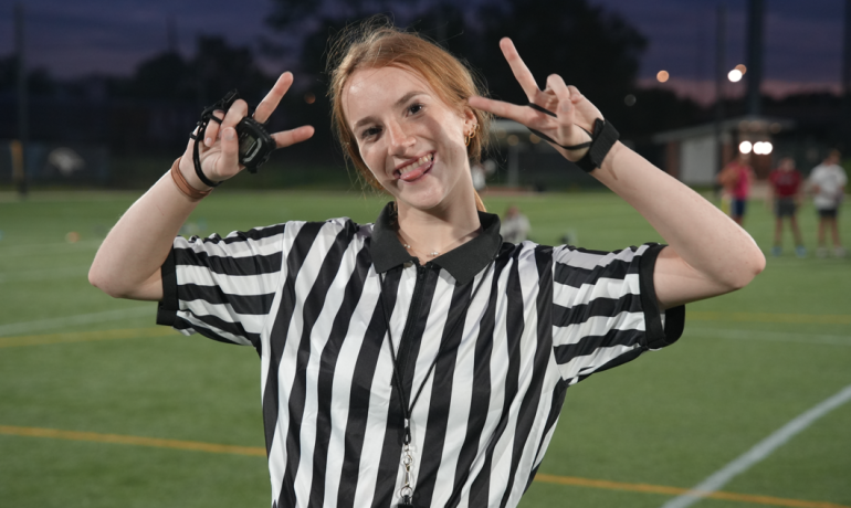 A young woman in a flag football officials uniform posing for the camera. 