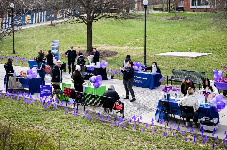 Tables and signs line a campus walkway during a recovery awareness event.