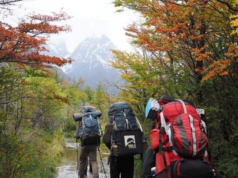 Hikers with backpacks crossing a stream toward snow-capped mountains in Patagonia, Chile