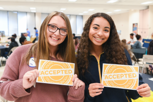 Two female students holding accepted signs 