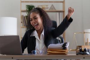 A woman looling at her computer excited about what she sees with her hand raised.