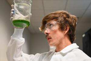 UTC science student looking at a beaker wearing goggles
