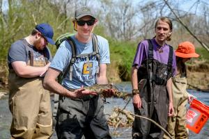 UTC Ichthyology students standing in a river wearing waiters holding a fish