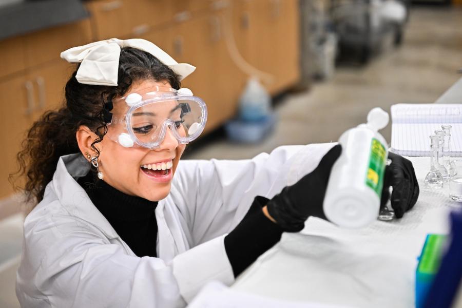 UTC student wearing a lab coat and goggles working with chemicals in a lab