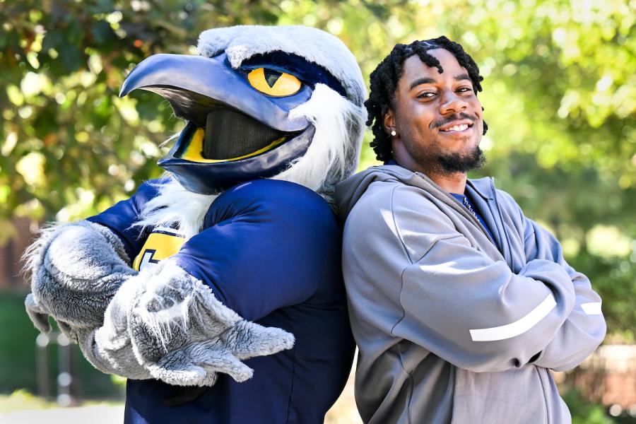 UTC student standing back to back with Scrappy, both with their arms crossed against their chest.