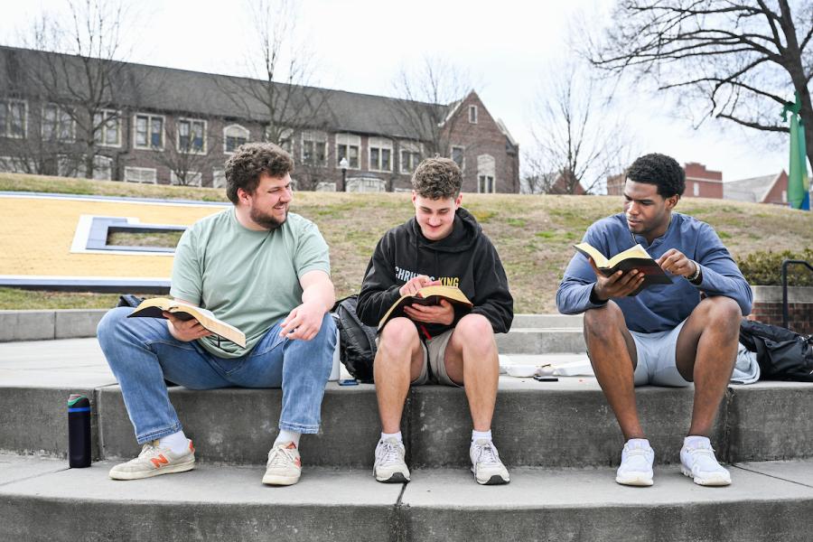Three UTC students reading books on Chamberlain Field