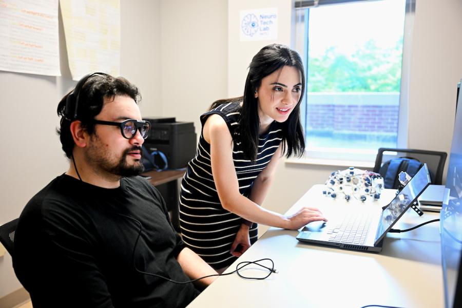 A woman showing a man results on a computer with experimental equipment in the background.