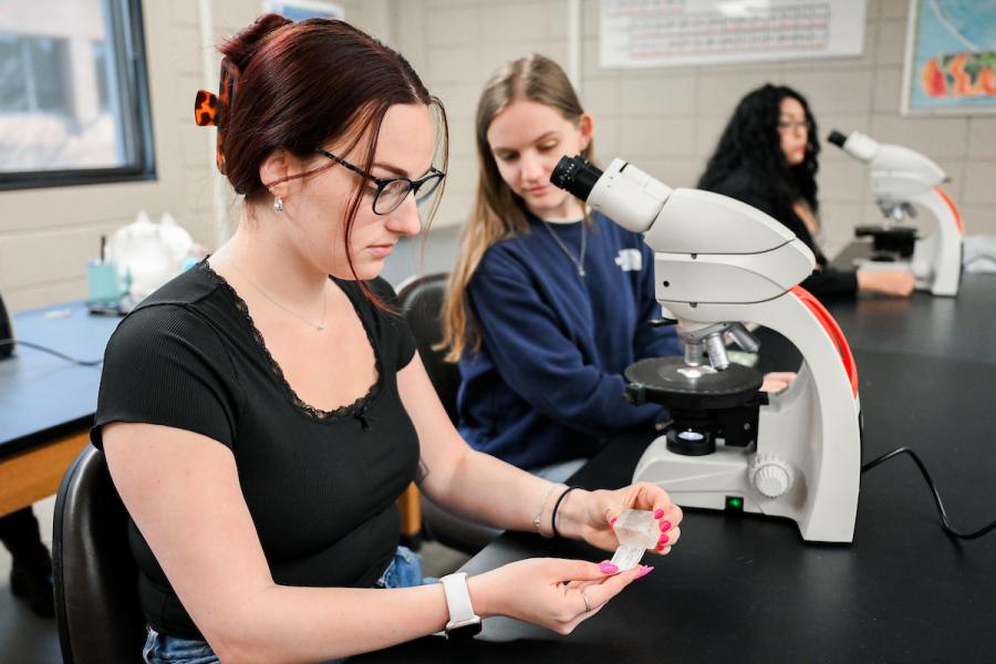 UTC female students putting together slides to look through a microscope