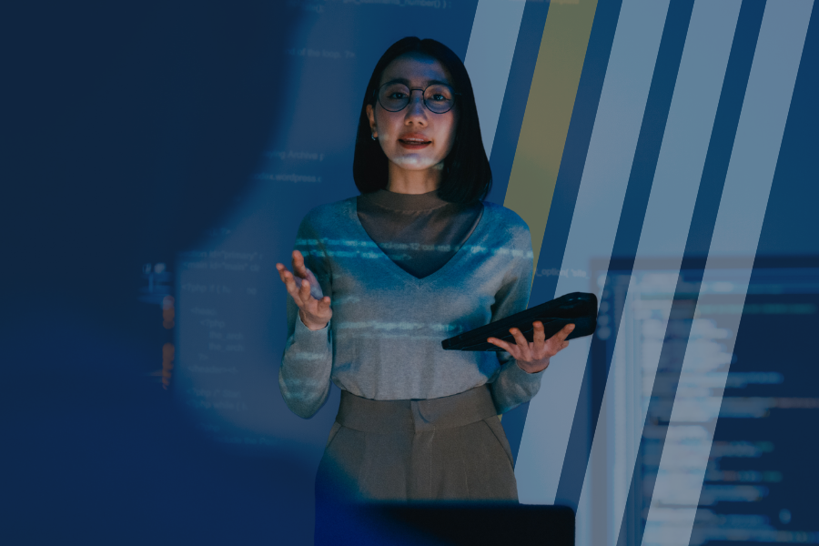 A woman stands in front of a room presenting data to co-workers. 