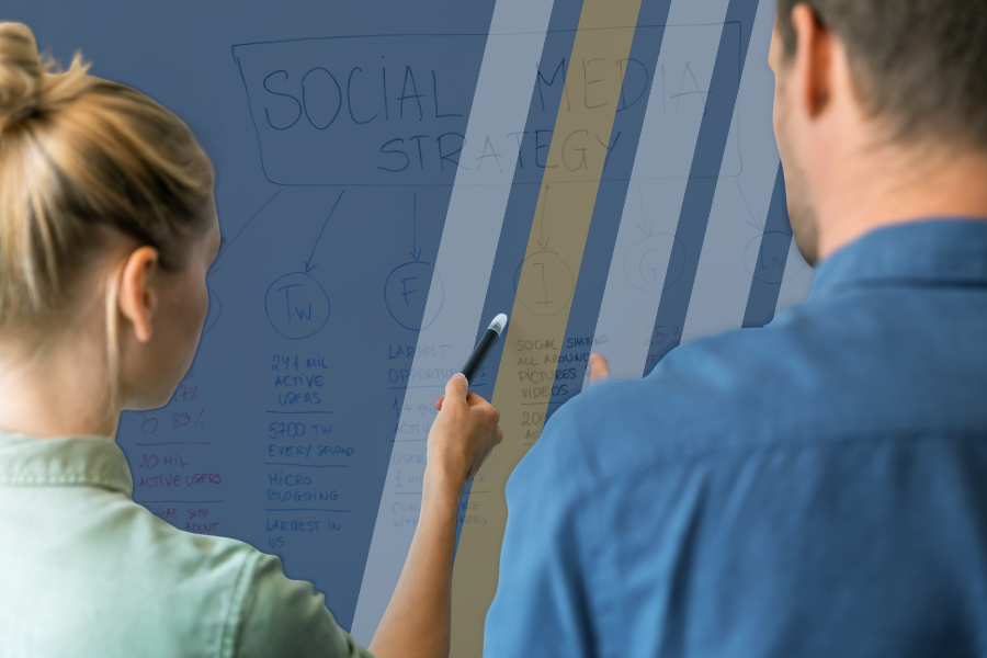 A woman and a man stand in front of a whiteboard discussing the social media strategy that is written on the board. 