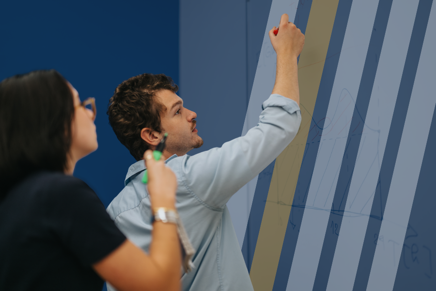 a student works an assignment on a whiteboard while another student looks on.