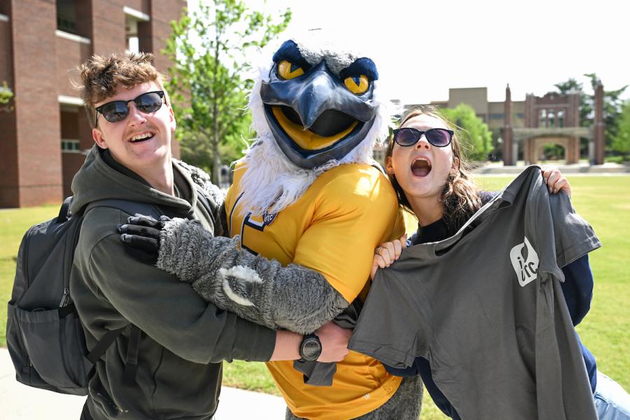 Two students holding shirts that say "I Love UTC" while standing next to Scrappy