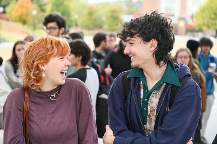 Two students laughing together on the UTC campus in front of a crowd of other students.
