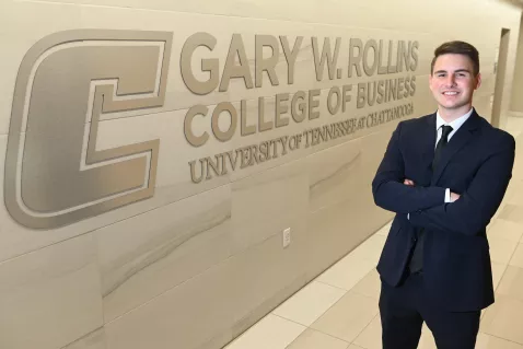 UTC Management student in front of the college of business logo